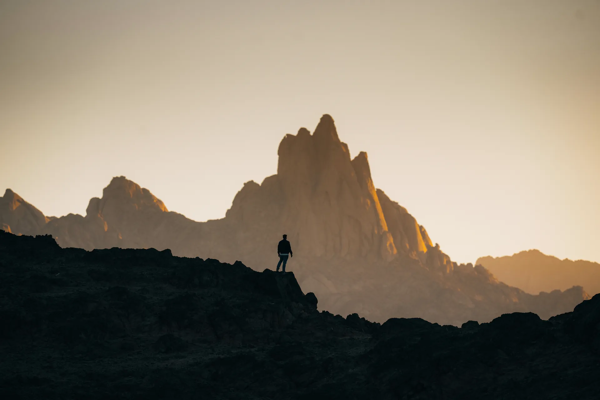 Figura in piedi su una cresta rocciosa che osserva una vetta illuminata dalla luce del tramonto